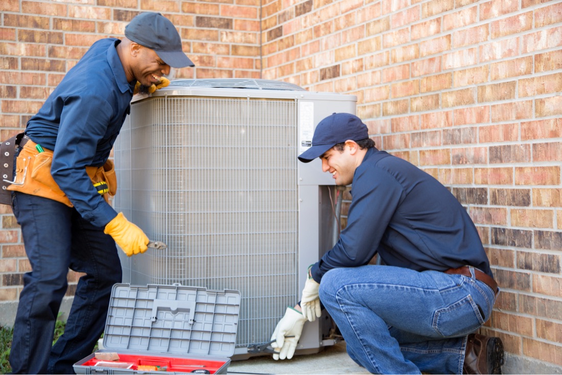 Two technicians working on an exterior HVAC unit