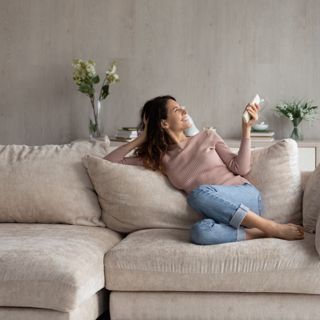 Female relaxing on couch, smiling with temperature control remote in hand